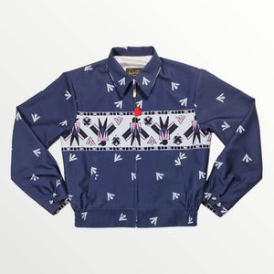 Puede incluir: Una chaqueta bomber azul marino con un patrón geométrico blanco y rosa en la parte delantera. La chaqueta tiene una cremallera y un cuello de pie.