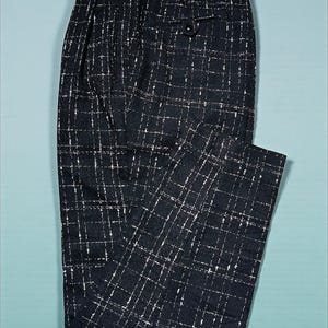 May include: Black and white checkered trousers. These pants feature a classic grid pattern with a button closure and a tailored fit. The fabric has a textured appearance, and the pants are laid flat on a light blue surface.