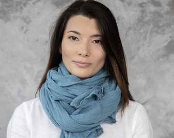 May include: A woman wearing a white shirt with a light blue linen scarf wrapped around her neck.
