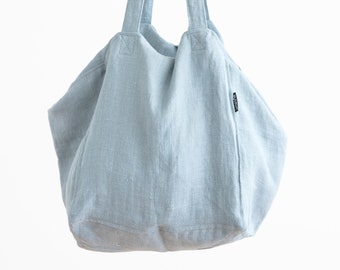 Può includere: Una borsa tote in lino blu chiaro con due manici lunghi. La borsa è vuota e ha una superficie leggermente strutturata.