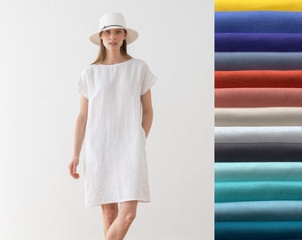 May include: A white linen dress with short sleeves and a scoop neck. The dress has a relaxed fit and falls to the mid-thigh. The model is wearing a white hat and sandals.