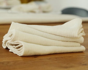 May include: A stack of four off-white linen napkins folded neatly on a wooden table.