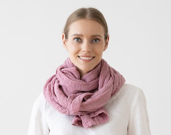 May include: A woman wearing a pink scarf around her neck. The scarf is made of a soft, textured fabric and is tied in a loose knot.