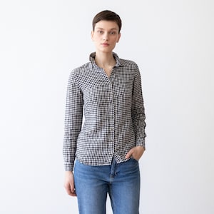 Puede incluir: Una mujer con una camisa de botones de cuadros blancos y negros de manga larga y pantalones vaqueros azules.