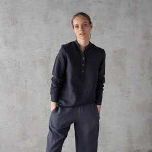 Puede incluir: Una persona lleva una camisa de lino azul oscuro con cuello abotonado y mangas largas. La camisa tiene un corte holgado y se combina con pantalones de lino azul oscuro a juego.