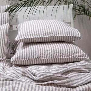 May include: Two gray and white striped linen pillowcases stacked on top of a gray and white striped linen sheet.