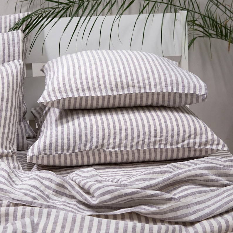 May include: Two gray and white striped linen pillowcases stacked on top of a gray and white striped linen sheet.