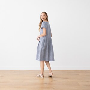 May include: A blue and white striped linen dress with short sleeves and a slightly flared skirt. The dress is knee-length and has a simple, casual style.