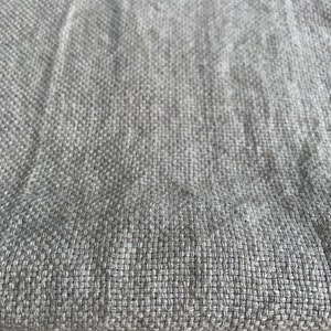 May include: Close-up of a light gray woven fabric with a subtle texture. The fabric has a smooth, even weave and a slightly rough feel.