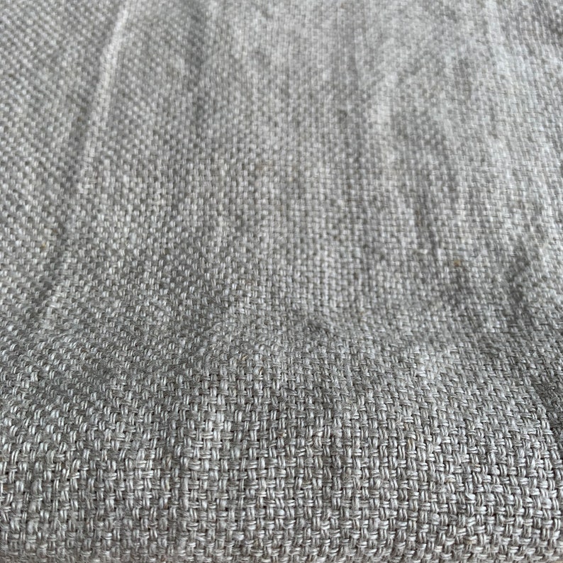 May include: Close-up of a light gray woven fabric with a subtle texture. The fabric has a smooth, even weave and a slightly rough feel.