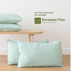 Może przedstawiać: Dwa jasnozielone poszewki z lnu na drewnianym stole. Poszewki są ułożone jedna na drugiej. W tle widoczny jest tekst "European Flax. Premium linen fibre".