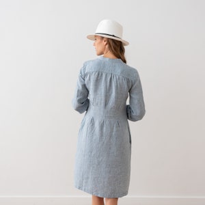 May include: A light blue linen dress with a white hat. The dress has a button-up front and long sleeves.