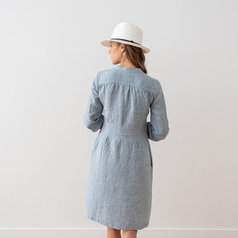 May include: A light blue linen dress with a white hat. The dress has a button-up front and long sleeves.
