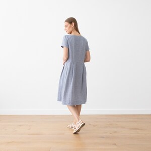 May include: A blue and white striped linen dress with short sleeves and a slightly flared skirt. The dress is knee-length and has a simple, classic design.