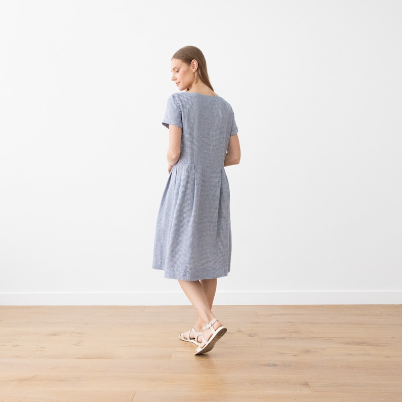 May include: A blue and white striped linen dress with short sleeves and a slightly flared skirt. The dress is knee-length and has a simple, classic design.