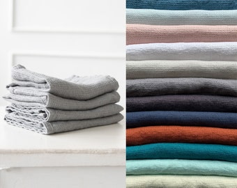 May include: A stack of five waffle weave towels in a light gray color. The towels are folded neatly and are displayed on a white table. A variety of colors of waffle weave towels are shown in the background.
