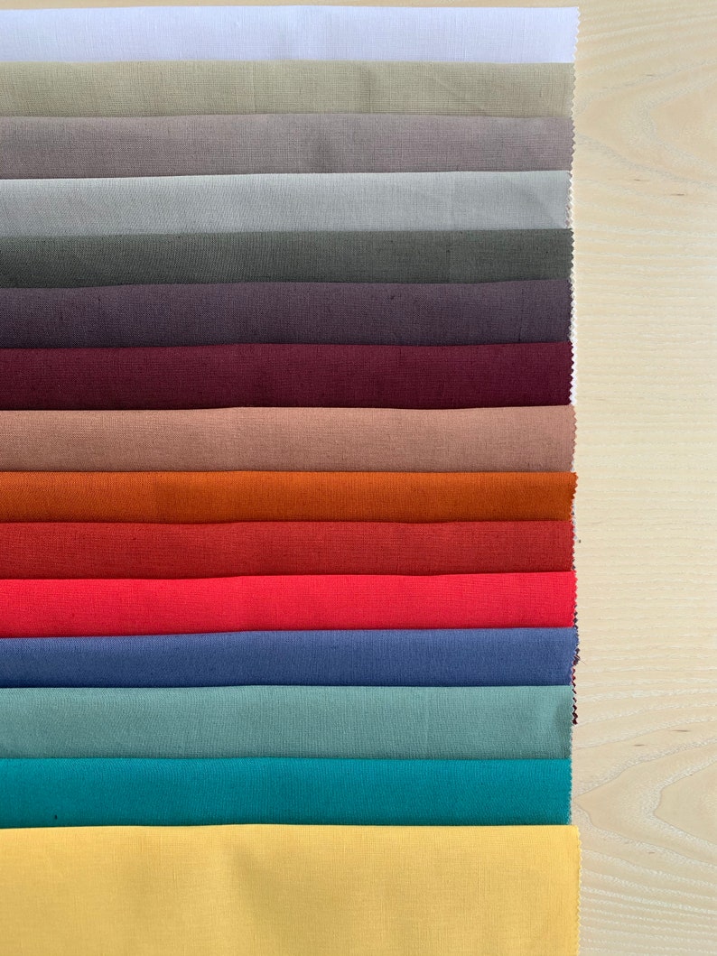 May include: A collection of 15 fabric swatches in various colors, including white, beige, gray, purple, maroon, brown, orange, red, pink, blue, teal, and yellow. The swatches are arranged vertically in a row, with the white swatch at the top and the yellow swatch at the bottom.