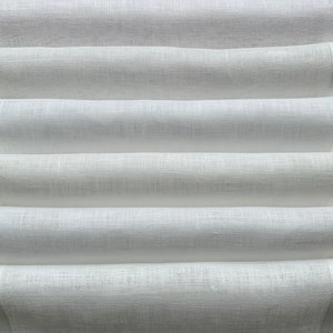 Puede incluir: Tela de lino blanco doblada en pliegues limpios y uniformes. La tela tiene una textura sutil y un aspecto suave y natural.