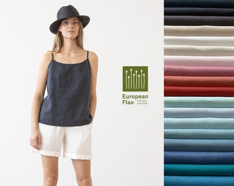 May include: A woman wearing a black linen tank top and white linen shorts. The tank top has a scoop neck and thin straps. The shorts have a relaxed fit and are cuffed at the hem. The woman is standing in front of a white background. The image also includes a logo for European Flax, a premium linen fiber.