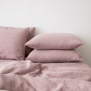 May include: A set of three dusty rose linen pillowcases stacked on top of a dusty rose linen duvet cover. The bedding is made of soft, natural linen and has a relaxed, casual look.