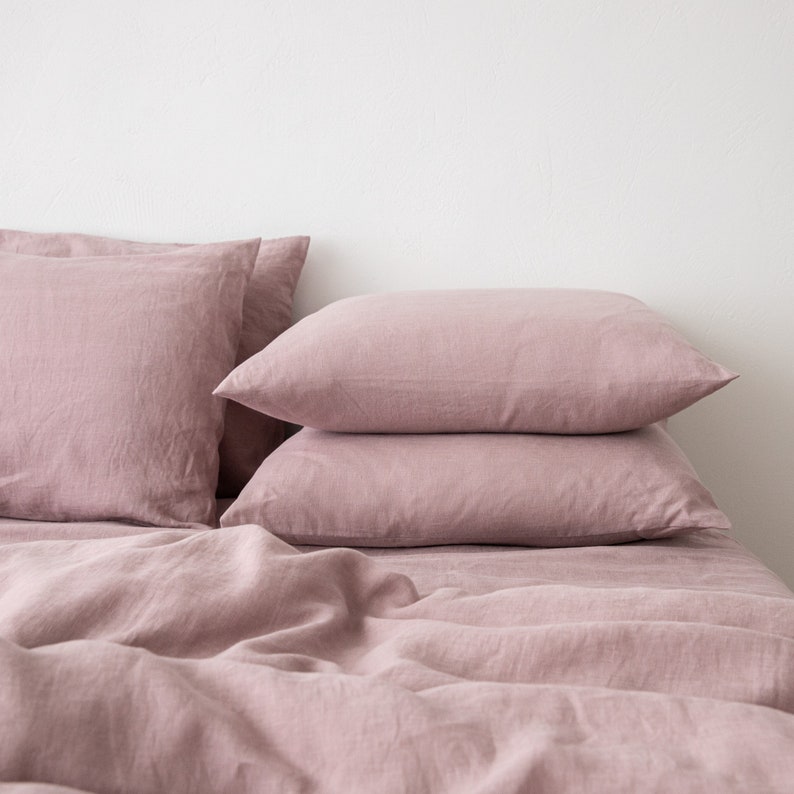 May include: A set of three dusty rose linen pillowcases stacked on top of a dusty rose linen duvet cover. The bedding is made of soft, natural linen and has a relaxed, casual look.