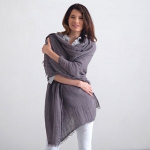 May include: A gray linen scarf with frayed edges. The scarf is draped around a person's neck and shoulders.