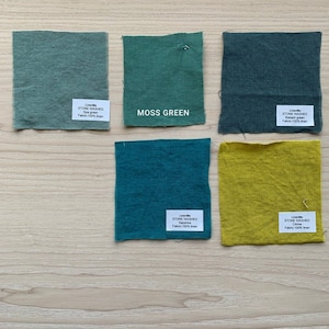 May include: Four fabric swatches in different shades of green and yellow. The swatches are labeled with the brand name "LinenMe" and the text "Stone Washed" followed by the color name. The colors are Spa Green, Balsam Green, Sapphire, and Cine.