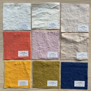 May include: Nine fabric swatches in various colors, including white, off-white, coral, lilac, latte, yellow, green, and blue. Each swatch has a label with the brand name "LinenMe" and the fabric type "TERRA&FRINGE".