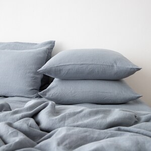May include: A stack of three blue linen pillowcases on a blue linen bedspread.