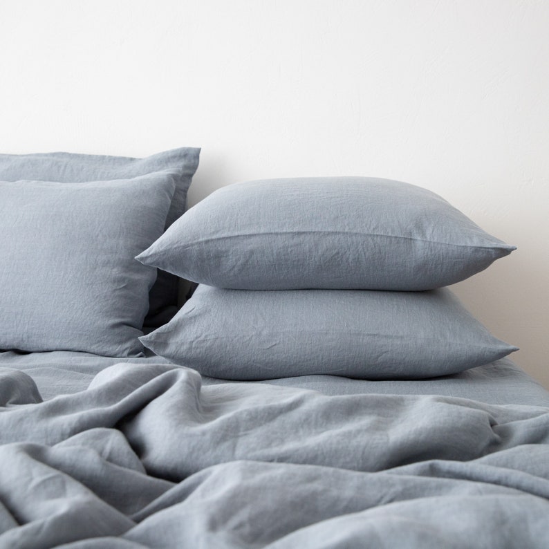 May include: A stack of three blue linen pillowcases on a blue linen bedspread.