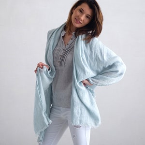 May include: A light blue linen scarf with frayed edges. The scarf is draped around a person's neck and shoulders.