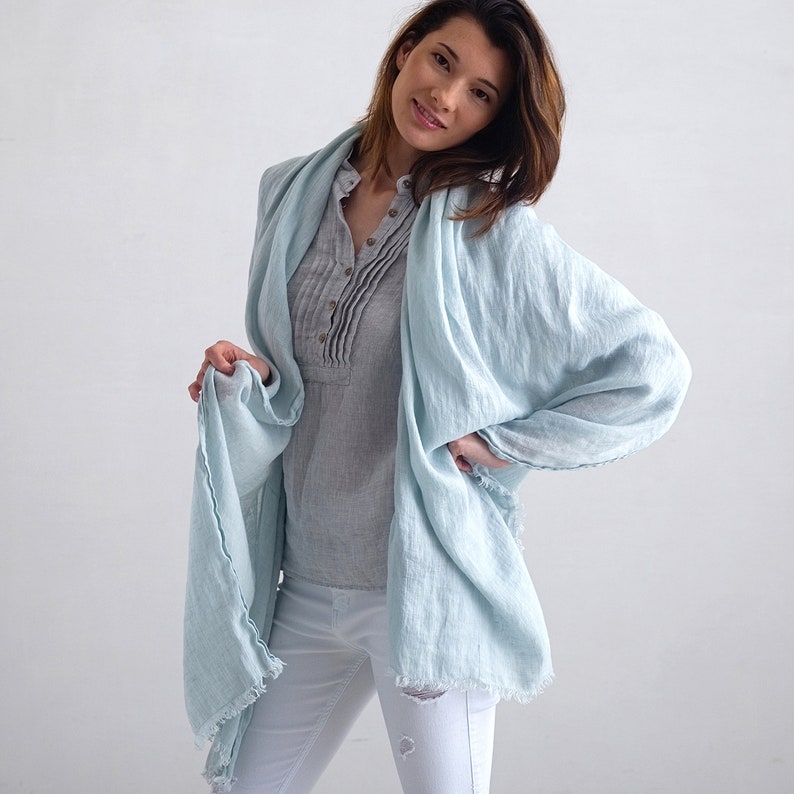 May include: A light blue linen scarf with frayed edges. The scarf is draped around a person's neck and shoulders.