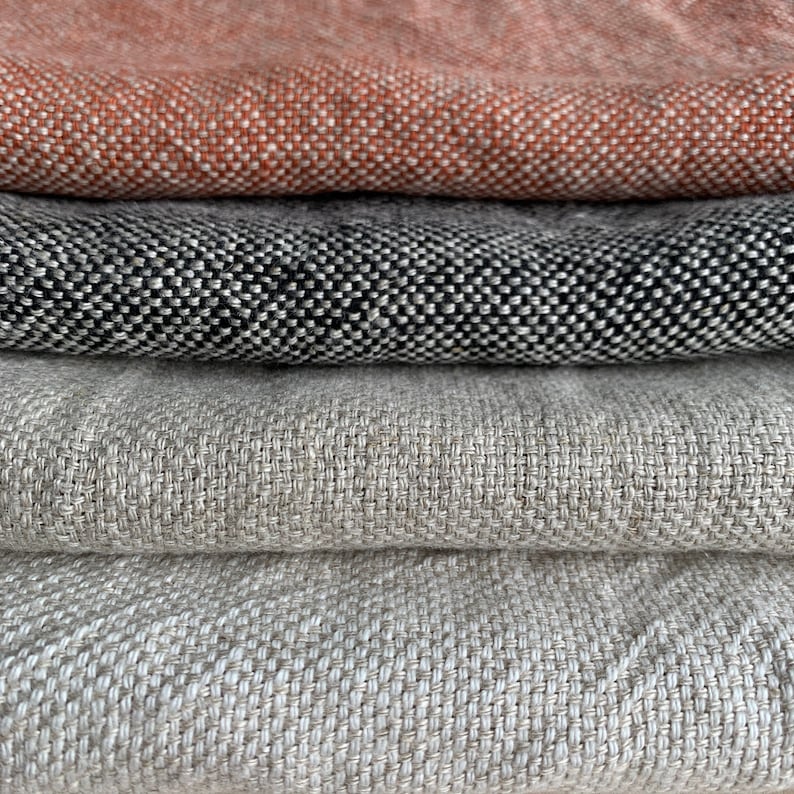 May include: Four fabric swatches stacked on top of each other. The top swatch is a light orange color, the second swatch is black with white flecks, the third swatch is a light beige color, and the bottom swatch is a slightly darker beige color.