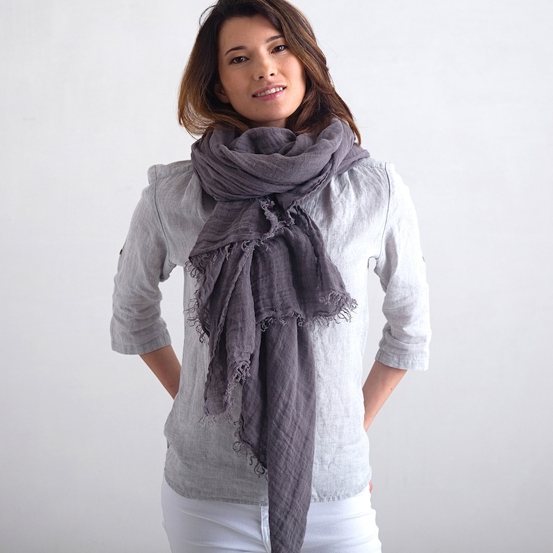May include: A woman wearing a white shirt and white pants with a gray linen scarf around her neck. The scarf is draped loosely and has a frayed edge.