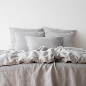 May include: A gray linen duvet cover and pillowcases with a wrinkled, relaxed look. The bedding is arranged on a bed with a white headboard.