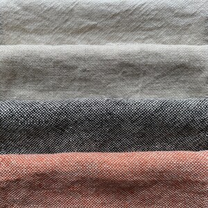 May include: Four fabric swatches stacked on top of each other. The top swatch is a light beige, the second swatch is a darker beige, the third swatch is a black and white tweed, and the bottom swatch is a rust orange.
