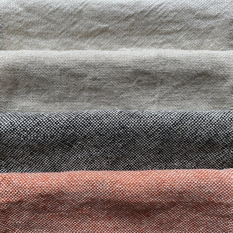 May include: Four fabric swatches stacked on top of each other. The top swatch is a light beige, the second swatch is a darker beige, the third swatch is a black and white tweed, and the bottom swatch is a rust orange.