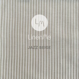 May include: Beige linen fabric with white stripes. The fabric has a subtle texture and a slightly rough feel. The fabric is labelled "LinenMe Jazz Beige".