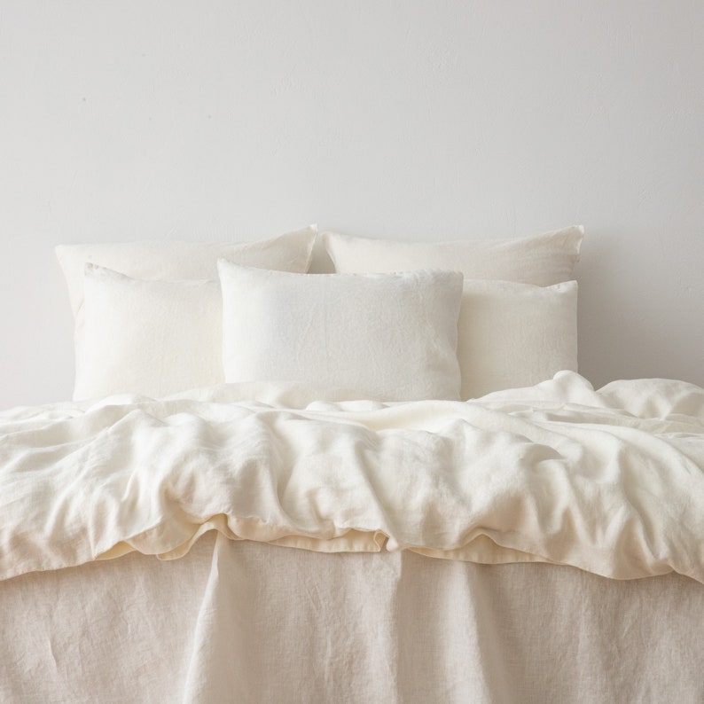 May include: A white linen duvet cover and pillowcases on a bed. The bedding is wrinkled and has a natural, relaxed look.