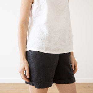 May include: A white sleeveless linen top paired with black linen shorts. The shorts have a cuffed hem.