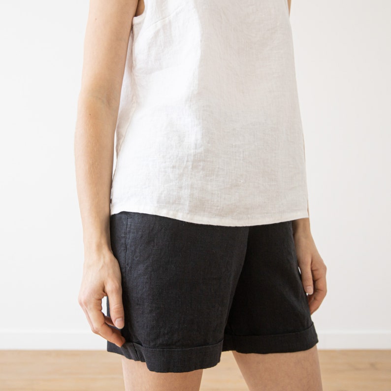 May include: A white sleeveless linen top paired with black linen shorts. The shorts have a cuffed hem.