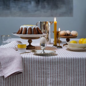 Peut inclure: Une nappe à rayures roses et blanches avec un porte-œuf en céramique blanche contenant un œuf blanc, une tasse à thé jaune, un pichet en argent, un support à gâteau avec un gâteau au citron et une assiette de citrons sur une table.