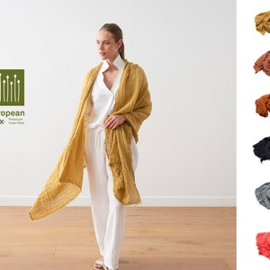 Peut inclure: Une femme porte une chemise blanche et un pantalon blanc, avec une écharpe en lin jaune drapé autour de son cou et de ses épaules. L'écharpe est faite de lin européen, une fibre de lin de qualité supérieure. L'image montre également cinq autres écharpes en lin de différentes couleurs : orange, marron, noir, gris et rose.