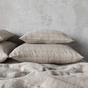 May include: A stack of four beige linen pillowcases with a red checkered pattern. The pillowcases are arranged on a bed with a matching linen duvet cover.