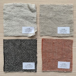 May include: Four fabric swatches in different colors and textures. The swatches are labeled with the brand name "LinenMe" and the text "Stone Washed". The colors are oatmeal, natural, black, and brick.