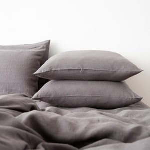 May include: A stack of three gray linen pillowcases on a gray linen bedspread.