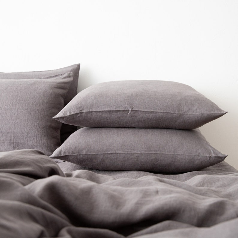 May include: A stack of three gray linen pillowcases on a gray linen bedspread.