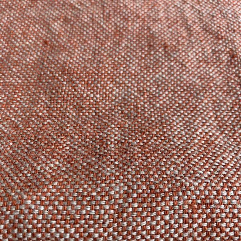May include: Close-up of a woven fabric with a textured pattern. The fabric is a mix of orange and white threads.