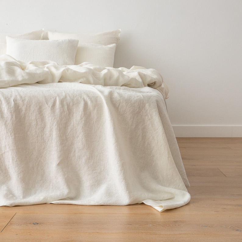May include: A white linen bedspread with a white linen duvet cover and two white pillowcases. The bedspread is draped over the foot of the bed.