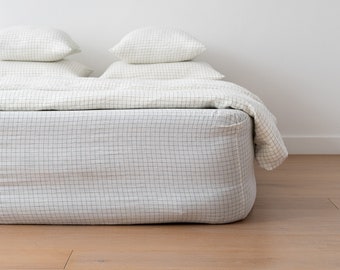 May include: White bed with a black and white checked fitted sheet and a white duvet cover. Two white pillows are on top of the duvet.